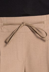 Pantaloni beige con una morbida texture del tessuto, dotati di un cordoncino in vita e tasche laterali, parte di una maglietta nera mostrata sopra.