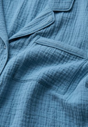 Veste en tissu bleu à texture avec un motif froissé subtil, dotée d'un col cranté et d'une poche poitrine unique. Matière douce.