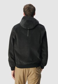 Czarna bluza z kapturem o miękkiej fakturze, z kontrastującymi szwami i żeberkowym wykończeniem, umieszczona na neutralnym tle.