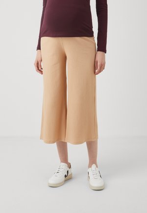 Beige ribbede culotter laget av mykt stoff, med et bredt ben-design. Kombinert med hvite sneakers prydet med svarte detaljer.