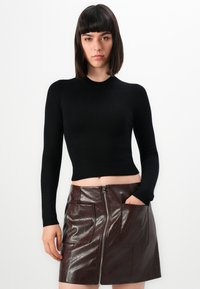 Maglietta nera attillata a maniche lunghe con orlo a costine, abbinata a una mini gonna in pelle lucida marrone con tasche frontali e zip centrale.