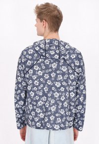 Jachetă cu glugă andurată florală în albastru marin cu flori albe. Are mâneci lungi, o croială lejeră și un material texturat.