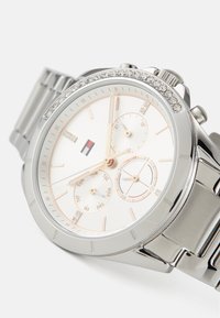 Montre-bracelet argentée avec un bracelet en acier inoxydable poli, un cadran blanc, des accents en or rose et une lunette ornée de cristaux.