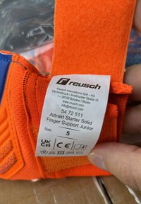 Reusch orange finger support with textured fabric, Velcro strap, and label detailing size 5 and product information.