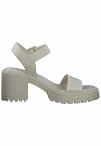 Beige blokhak sandalen met een gestructureerde zool, voorzien van een brede elastische band over de voorkant van de voet en een gesp sluiting bij de enkel.