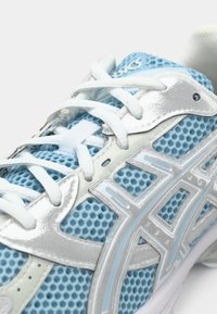 Hellblaue Sportschuh mit Netzmaterial, silbernen Akzenten, strukturierten Überzügen und weißen Schnürsenkeln. Mit ASICS-Logo auf der Zunge.