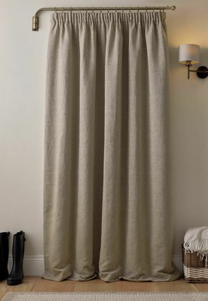 Tenda di lino beige appesa a un'asta di ottone vicino a stivali neri su pavimento in legno e un cestino intrecciato con una coperta bianca sotto una lampada da parete.