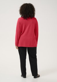 Haut rouge à manches longues avec une coupe droite, associé à un pantalon noir. Le tissu semble doux et le design présente un col simple.