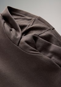 Donkerbruine gevouwen hoodie die capuchon en naden toont op een effen lichte achtergrond, met nadruk op de textuur van de stof en stikseldetails.