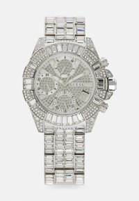 Montre Guess en argent avec un cadran blanc, un rehaut incrusté de cristaux, des fonctionnalités de chronographe et un bracelet en acier inoxydable à motifs.