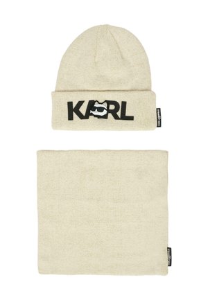 Beige gebreide beanie met "KARL" in zwarte letters en een cartoon gezicht logo; inclusief bijpassende beige nekwarmer. Beide hebben een zachte textuur.