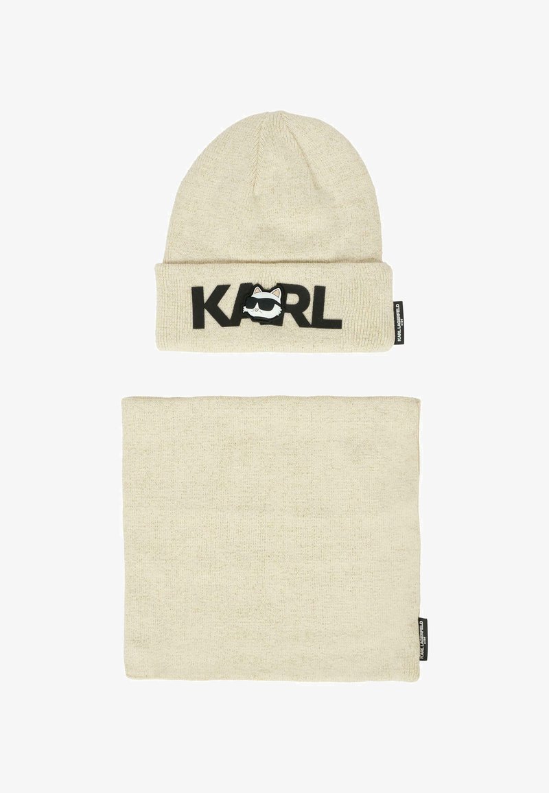 Beanie beige lavorata a maglia con "KARL" in lettere nere e un logo con un faccino di cartone; include un caldo scaldacollo beige abbinato. Entrambi hanno una texture morbida.