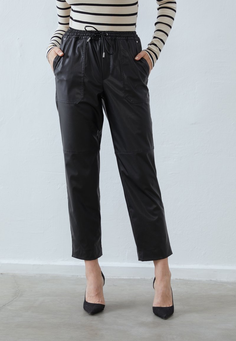 Pantalon jogger en similicuir noir avec une taille élastique, des poches latérales et une longueur raccourcie. Présente une texture lisse et des lignes épurées.