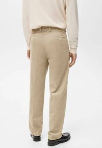 Pantalones de pana beige con un diseño de pierna recta, que presentan sutiles crestas verticales y dos bolsillos traseros. Combinados con un suéter claro y zapatos negros.