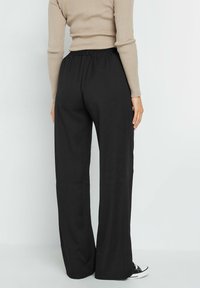 Zwarte wijde broek met een elastische tailleband, gemaakt van een zachte stof, met een gladde textuur en een minimalistisch ontwerp.
