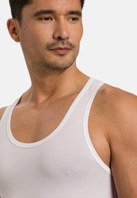 Bílý bavlněný top bez rukávů s kulatým výstřihem a širokými ramínky, s hladkou strukturou a minimálním švem.