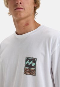 White long-sleeve t-shirt with a multicolored graphic featuring waves and text on the left chest area. Soft cotton material.
