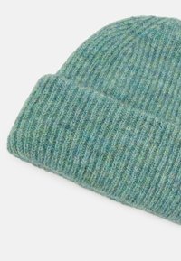 Knit beanie in a soft, textured yarn with a blend of light and dark green tones. Features a rolled cuff and a rounded top.