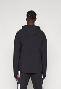 Zwarte capuchonjas met lange mouwen, gemaakt van lichtgewicht materiaal. Heeft een eenvoudig ontwerp, met een gladde textuur en geen zichtbare patronen.