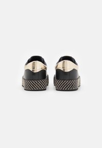 Scarpe platform in pelle nera con un raffinato accento oro lucido sul tallone e una suola con texture a righe bianche e nere.