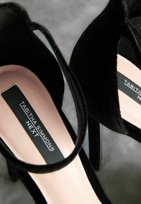 Scarpe con tacco alto in suede nero, con fasce alla caviglia e una soletta morbida rosa. Logo visibile sulla soletta, che mette in risalto i dettagli del marchio.