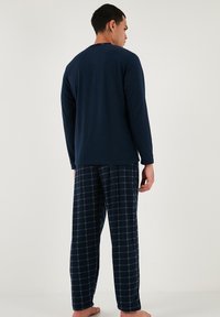 Tricou cu mânecă lungă navy, cu decolteu rotund, asociat cu pantaloni cu model tartan în nuanțe de navy și alb. Material din bumbac moale, croi lejer.