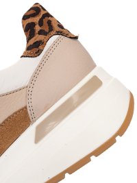 Plano detalle del talón de una zapatilla beige y blanca con un detalle de tela con estampado de leopardo y una suela gruesa blanca con dibujo de goma color caramelo.