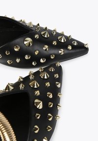 Black pointed-toe shoes made of synthetic leather, featuring gold metal spikes of varying sizes across the surface.