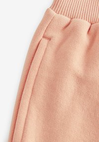 Peachfarvede joggere lavet af blødt stof, med ribbet talje og en subtil tekstur samt synlige sidelommer.