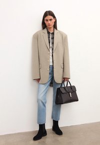 Beige oversized blazer med två knappar, rutigt skjorta under, ljusblå jeans, svarta ankelstövlar och en svart handväska. Släta ytor.