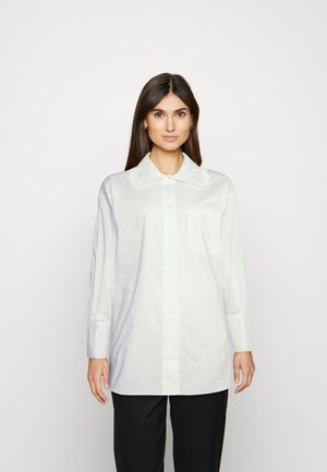 Camisa branca de botão com um grande colar texturizado, mangas longas e um bolso no peito. Feita de um tecido leve e suave.