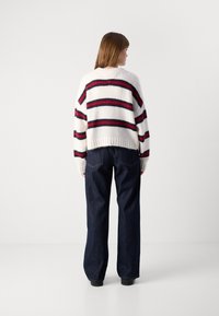 Maglione a maglia con righe orizzontali bianche, rosse e blu navy, vestibilità morbida, orlo a coste. Abbinato a pantaloni a gamba larga in denim scuro a vita alta.