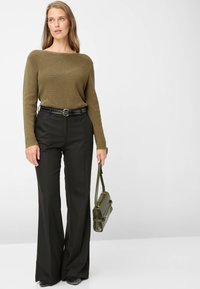 Olijfgroene geribbelde trui, zwarte broek met wijde pijpen en een riem, en een groene handtas, met gladde materialen en eenvoudige hardware-accenten.