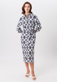 Robe midi à motifs bleu marine et blanc avec un col de chemise, des manches bouffantes longues et une ceinture à nouer à la taille. Texture de tissu lisse.