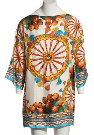 Tunica bianca larga con maniche larghe caratterizzata da motivi circolari colorati, fichi d’India arancioni e nappe multicolori su un bordo azzurro chiaro.