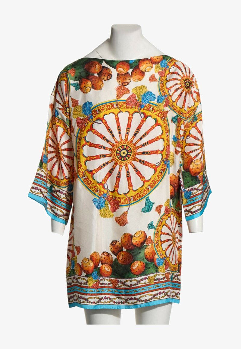 Tunique blanche ample à larges manches ornée de motifs circulaires colorés, de figues de barbarie orange et de pompons multicolores sur une bordure bleu clair.