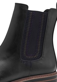 Bottine en cuir noir à cheville avec panneau latéral élastique, arborant un motif texturé violet et marron. Détail cousu autour de la semelle.