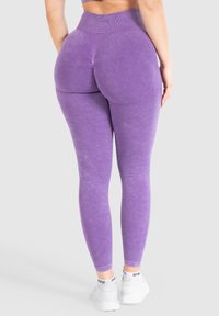 Leggings viola a vita alta realizzati in tessuto elasticizzato, con vita a coste e design sagomato. Abbinati a sneaker bianche.