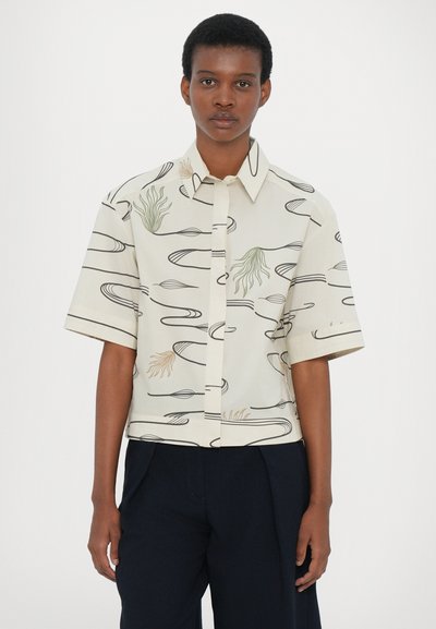 Camicia a maniche corte di colore crema con motivi astratti a linee verdi e marroni, chiusura con bottoni sul davanti e vestibilità comoda.