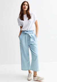 Ljusblå vida byxor med bälte i midjan, gjorda av denim. Kombinerat med en vit t-shirt med kort ärm och beige sneakers.