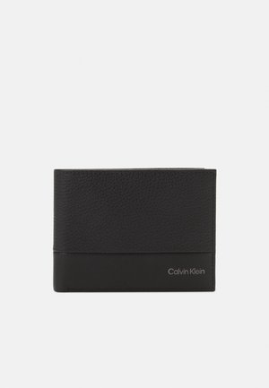 Portafoglio in pelle nera con una sezione superiore testurizzata, sezione inferiore liscia e un logo "Calvin Klein" in argento in basso a destra.