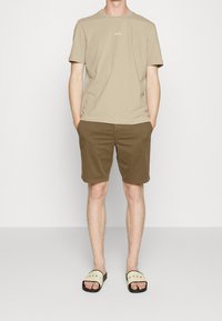 Béžové bavlněné tričko s logem "BOSS", hnědé bavlněné šortky a krémové sandály na klínku s červeným nápisem. Jednoduchý, ležérní letní outfit.