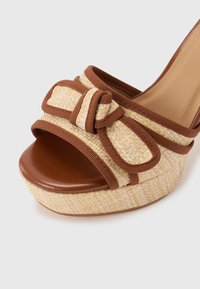 Πλατφόρμα σανδάλι με σφήνα, πλεγμένη από άχυρο και καφέ περίγραμμα, με καφέ ανοικτή μύτη και διακοσμητικό φιόγκο στο λουράκι.