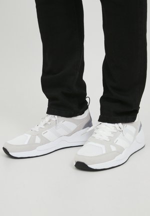 Witte en grijze sportieve schoenen van mesh en suede, met een gestructureerde zool en contrasterende accenten, gedragen met zwarte broek.