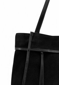 Sac cabas en daim noir avec une lanière et des détails en cuir lisse, présentant une forme propre et structurée ainsi qu'une texture douce.