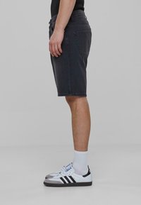 Donkergrijze denimshorts met een rechte pasvorm, voorzien van zijzakken en zichtbare stiksels. Gecombineerd met witte sneakers en sokken tot aan de enkel.