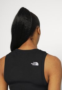 Czarny bezrękawnik o żeberkowej fakturze z białym logo "The North Face", widok z tyłu.
