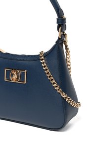 Granatowa torebka wykonana z teksturowanej wegańskiej skóry, z akcentem w postaci złotego logo oraz odpinanym złotym paskiem na łańcuszku. Charakteryzuje się zarysowaną sylwetką.