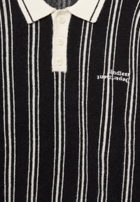 Maglietta polo a strisce bianche e nere con collo classico, patta con tre bottoni e testo ricamato sottile sul petto.