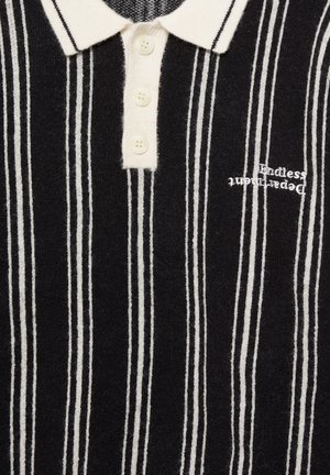 Črno-bela polo majica z navpičnimi črtami, ki ima klasičen ovratnik, ploskev s tremi gumbi in subtilen vezen napis na prsnem delu.